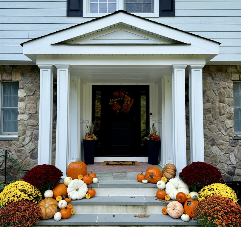 White-columned stone front entry in Des Moines styled with mums and layered classic and heirloom pumpkins by Front Porch Collective