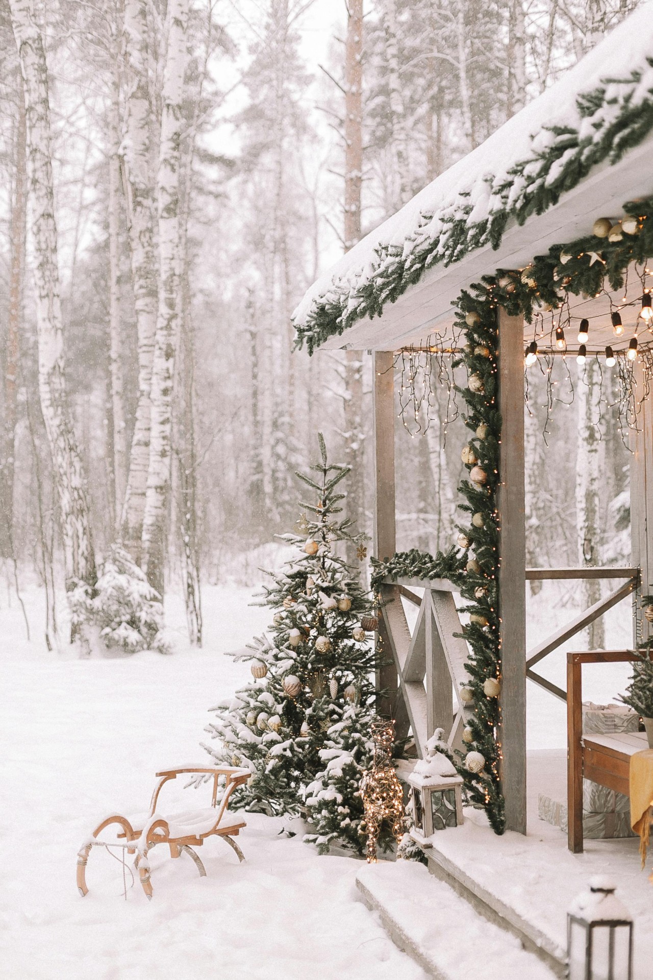 Snowy porch with Christmas garland, lights and decorated tree